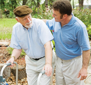 Male patient advocate walks down path with his arm around his elderly male client (who is using a walker)